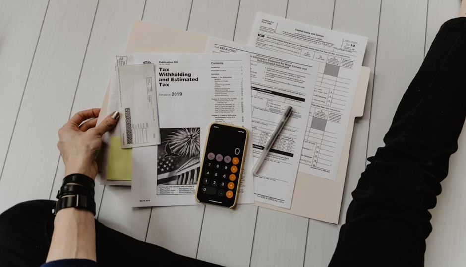 Person reviewing IRS tax forms with phone calculator and documents.

